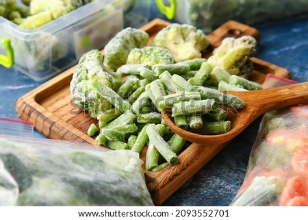 Wooden board with different frozen vegetables on color background
