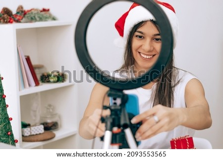 Woman blogger influencer in a santa claus hat talking smartphone live recording video blog on social network at home.Social media live streaming.New Year,Christmas concept.