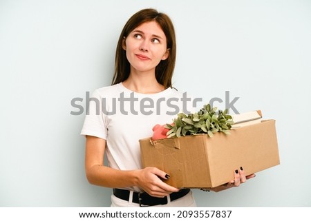 Young English woman making a move while picking up a box full of things isolated on blue background dreaming of achieving goals and purposes