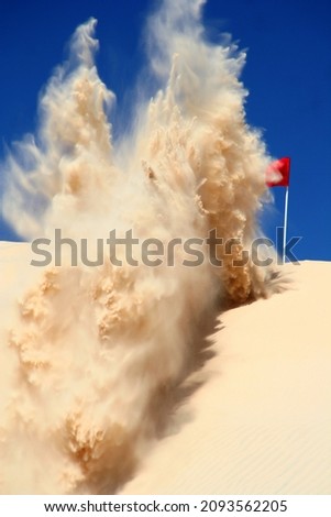 Sand explosion in the sand dunes as the sand flies up in the air.
Kicked up by a quad bike digging into the sand.