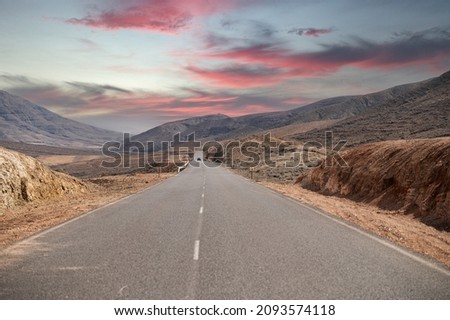 Empty asphalt road going through dry mountainous terrain under cloudy sunset sky in summer evening in Fuerteventura, Canary Island, Spain Royalty-Free Stock Photo #2093574118