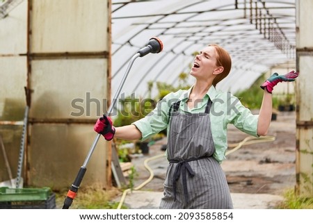 Young woman as a gardener trainee sings exuberantly into a hose in the nursery Royalty-Free Stock Photo #2093585854