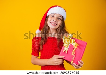 cute cheerful girl in a Christmas hat on a colored background holding a gift