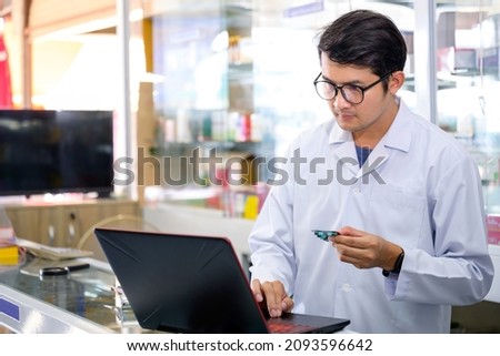 Young Asian male pharmacist checking drugs in pharmacy inventory using a computer at a pharmacy high quality photos