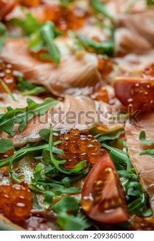 Delicious hot pizza with salmon, red caviar, tomatoes and aragula. Food recipe background. Close up, top view.
