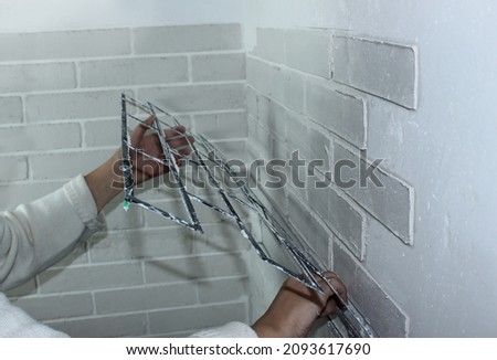 Close-up - a woman's hand removes the stencil from the decorative plaster on the wall. House renovation, decorative brick-like plaster on the wall. Make a brick wall at home with your own hands Royalty-Free Stock Photo #2093617690