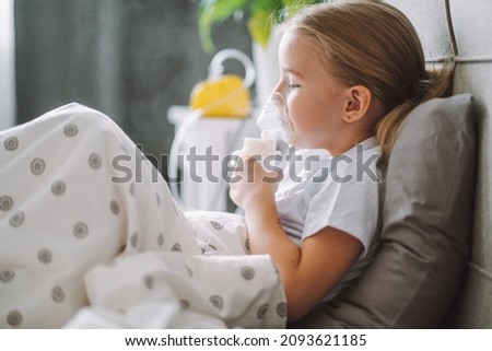 Little girl use inhaler nebulizer lying in bed in bedroom. Child asthma inhaler, nebulizer steam, flu or cold concept. Copyspace Royalty-Free Stock Photo #2093621185