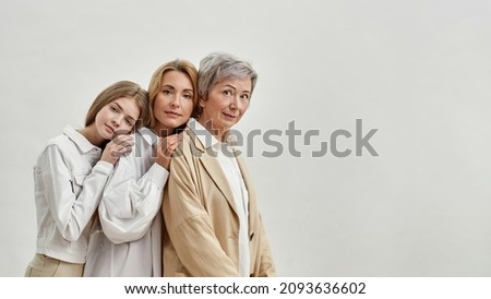 Side view of back to back of serious caucasian family of three female generations looking at camera. Age and generation concept. Senior and adult women with teenage girl. White background. Copy space Royalty-Free Stock Photo #2093636602