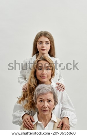 Row of serious caucasian family of three female generations looking at camera. Family generation change concept. Grandmother, mother and granddaughter. Isolated on white background. Studio shoot Royalty-Free Stock Photo #2093636860