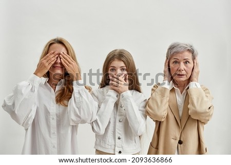 Caucasian family of three female generations showing gestures of three wise monkeys. Grandmother covering ears. Mother covering eyes. Granddaughter covering mouth. White background. Studio shoot