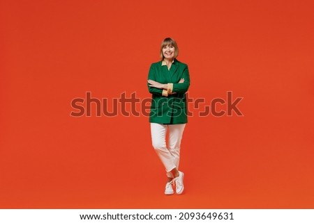 Full body elderly smiling happy cool confident woman 50s in green classic suit hold hands crossed folded isolated on plain orange color background studio portrait. People business lifestyle concept
