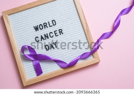 Purple ribbon as symbol of World Cancer Day over pink color background