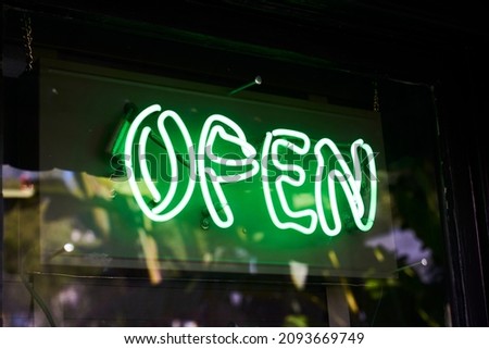 Green neon open sign hanging in a window with reflections