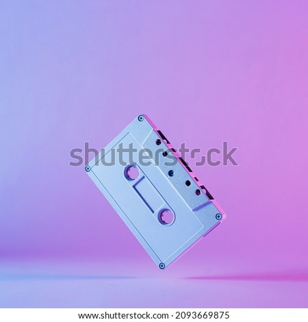Colorful artistic still life of an old audio cassette balancing in edge over a graduated purple background