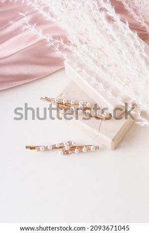 Two golden hair clips with pearls on marble background. Silk pink fabric and dried flowers. Jewelry for bride