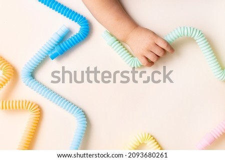 Trendy kids toys pastel colorful pop-tube in baby toddler hands on beige background. Set of forms and colors corrugated pipe and anti stressing, relaxation fidget finger toys. 