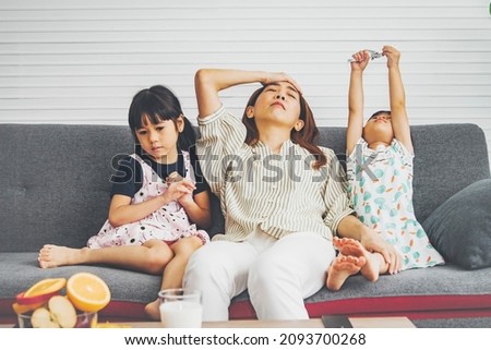 Stressful mother with a daughter who is hard to obey : Headache and tired housewife and her two mischievous, playful, playful little daughters are together on a week-end vacation at home. Royalty-Free Stock Photo #2093700268