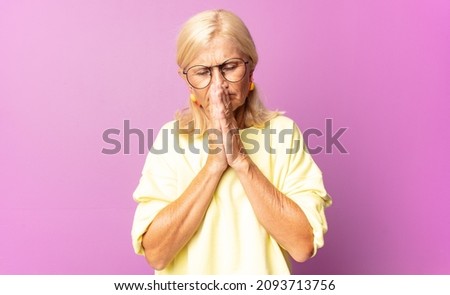 middle age woman feeling worried, hopeful and religious, praying faithfully with palms pressed, begging forgiveness