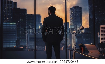 Thoughtful Young Businessman in a Perfect Tailored Suit Standing in His Modern Office Looking out of the Window on Big City in the Evening. Successful Finance Manager Planning Project Strategy. Royalty-Free Stock Photo #2093720665