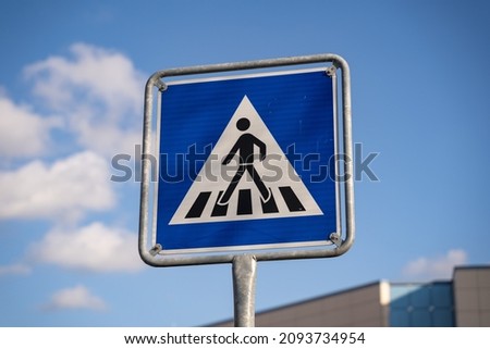 Pedestrian crossing traffic sign in Germany. Person walking on zebra stripes on a blue square road sign. Rules for car drivers on the street. Warning to call attention to people crossing the way.