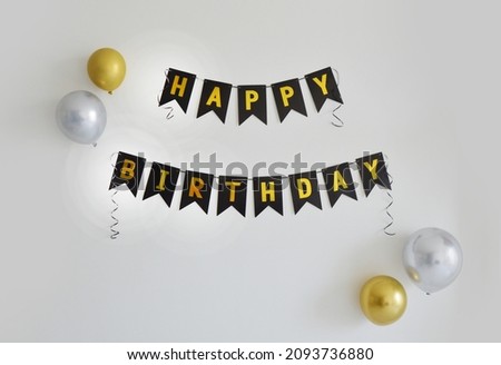 Golden and black Happy Birthday banner on white wall with silver and gold balloons