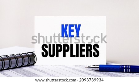 On a light gray background, a notebook, a blue pen and a sheet of paper with the text KEY SUPPLIERS. Business concept