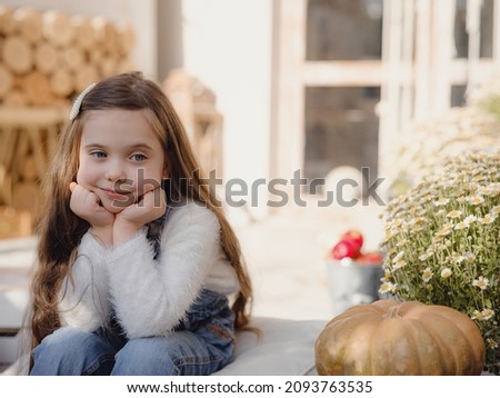 Happy little girl sitting on porch of house. home fall decoration for Thanksgiving. Smilling Child in autumn garden with yellow pumpkins