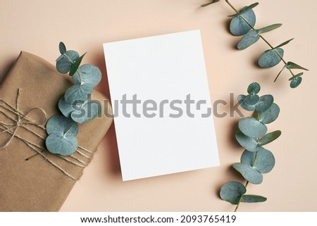 Greeting card mockup with gift box and natural eucalyptus twigs on paper background