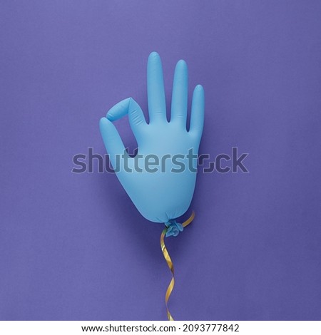 Blue Latex Medical Gloves as Balloon on violet background, shows character okay. colored in Very Peri - color of year 2022. Minimalism concept.