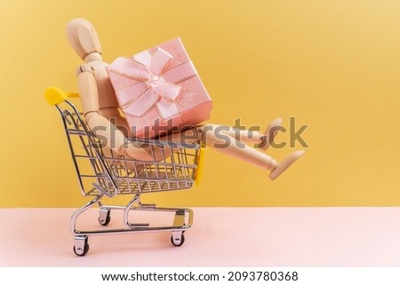 Wooden Mannequin with shopping cart with big Gift Box. Online Shopping Concept. Christmas Sales or gift shopping.
