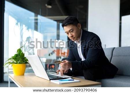 Portrait thoughtful Asian businessman working on a laptop computer at a modern office desk. Confident Focused pensive man in formal suit indoors. thinking of inspiration solving a problem. Startup