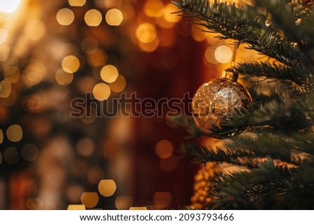 Golden shiny magic Christmas ball hanging on the Christmas tree branches. Winter holiday fairy garlands illumination and festive details in the interior