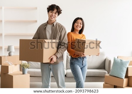 Portrait of young Asian woman and her cool boyfriend holding cardboard boxes, looking at camera and smiling in new home. Millennial spouses moving and settling into rented apartment Royalty-Free Stock Photo #2093798623