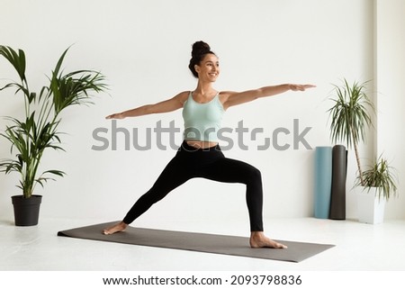 Beautiful Young Woman Practicing Yoga, Standing In Warrior Pose On Fitness Mat, Attractive Millennial Female In Sportswear Training In Light Studio, Enjoying Healthy Lifestyle, Copy Space Royalty-Free Stock Photo #2093798836