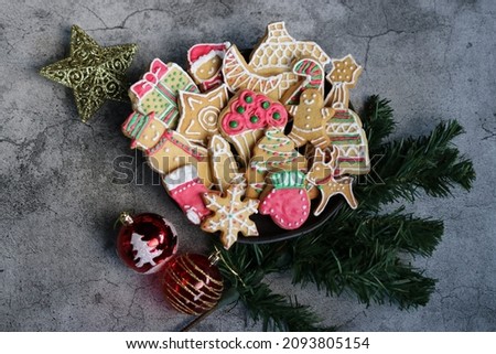 Gingerbread cookies in the shape of Christmas trees, moons, stars, shoes, bells, snowmen,  coated with white, green, and red icing on a cement background.