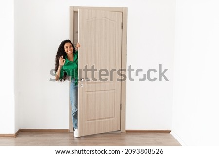 Good Offer. Portrait of cheerful young lady standing in doorway of her apartment, smiling millennial female homeowner holding ajar door looking out, greeting visitor, showing okay cool sign gesture