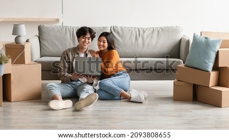 Loving young Asian couple with laptop buying household goods for their new home online, sitting on floor with pc on moving day, copy space. Millennial homeowners planning their house design online Royalty-Free Stock Photo #2093808655