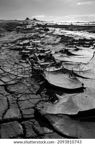 Black and white picture of drying mud in scales-like pattern with small volcanic cones in the background at Berca Mud Volcanoes reservation