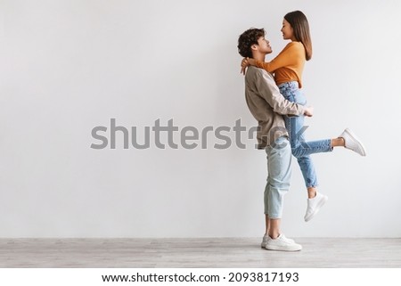 Side view of romantic young Asian guy holding and hugging his beloved girlfriend against white studio wall, copy space. Full length fo millennial spouses expressing love and affection Royalty-Free Stock Photo #2093817193
