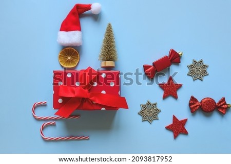 Christmas background with Santa hat, gift box, dry spices, orange rings, cinnamon, candies, sleigh against blue background. Top view. Flat lay. New Year mood. Greeting card. holiday celebration 