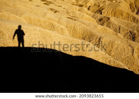 Man shadow silhouette projected over a dried mud ravine yellowed by the setting sun at Berca Mud Volcanoes reservation