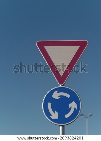 Vertical shot of a yield and roundabout traffic sign attached on a metal pole against a blue sky