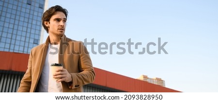 stylish man in coat holding coffee to go with buildings and sky at background, banner	