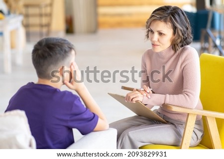 Upset teenager holding his head. Middle-aged woman psychologist talks to him. Mental health. School psychologist. Against background of light office. Royalty-Free Stock Photo #2093829931