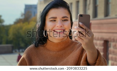 Portrait happy young woman in city outdoors photographed takes selfie blogging pretty Hispanic girl blogger talking smiling conference by phone device shoots video for vlog photo on mobile camera