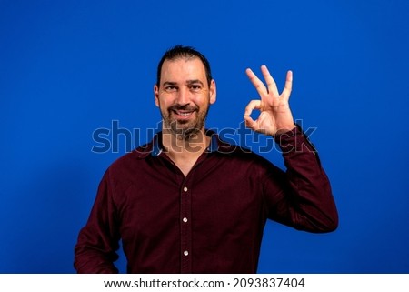 Photo of funny macho guy showing okey symbol expressing agreement and positive attitude wear casual shirt isolated blue color background
