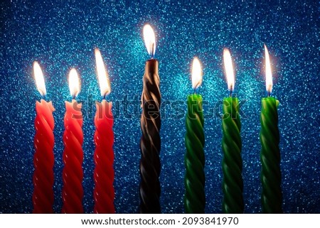 Celebration of African American Kwanzaa holiday. Seven burning candles in traditional kinara candlestick on blue glittering background.