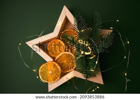 Christmas decor with wooden plates in the shape of a star, branches of a Christmas tree and dried oranges on a green background. Christmas card. Top wiev.