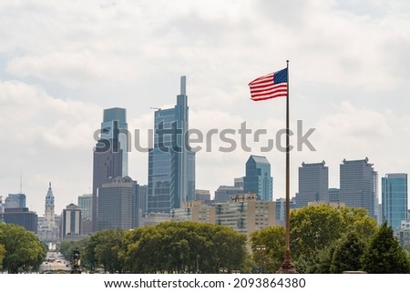 Skyline of Philadelphia financial downtown and City Hall Clock Tower at summer day time, Pennsylvania, USA. Hovering United States flag on the hot wind blow.