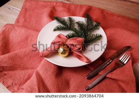 Christmas dinner. Christmas Day. Christmas branches with white empty plate, red napkin and cutlery on wooden background. Christmas day. New Year background. Red napkin in the shape of a bow.